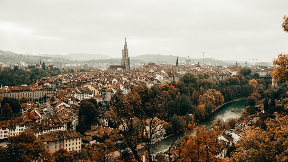 Scenic aerial photograph of Bern's historic old town during autumn, featuring the Cathedral of Bern and Aare River.