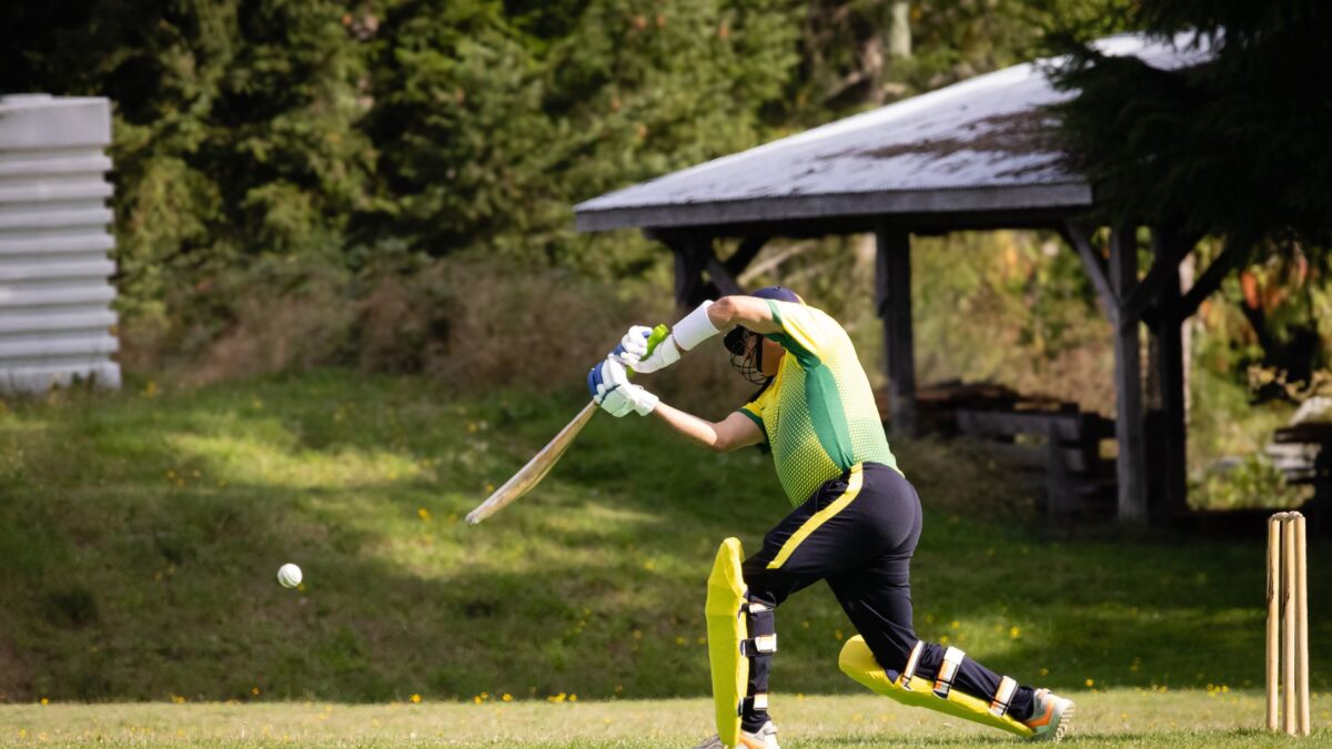 Cricketer playing a dynamic shot in a vibrant outdoor setting during a match.