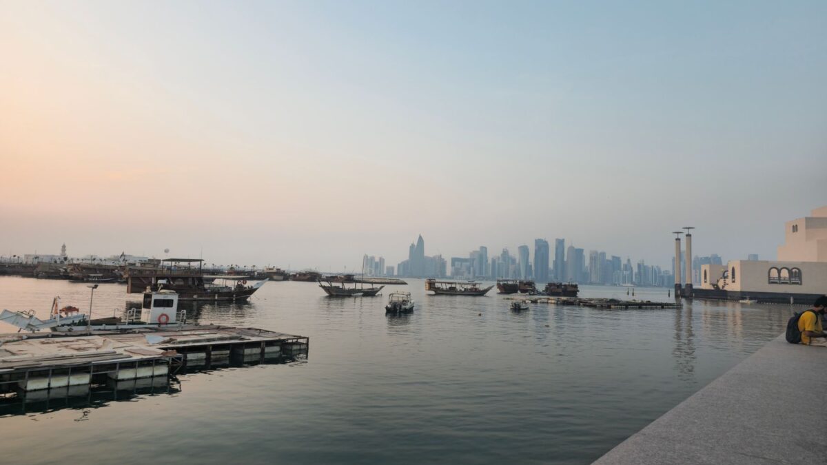 Scenic sunset view of Doha skyline from Corniche with traditional boats and calm water.