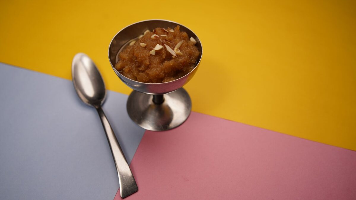 A vibrant photo of traditional Indian dessert Gajar Halwa served in a silver cup on a multicolored background.