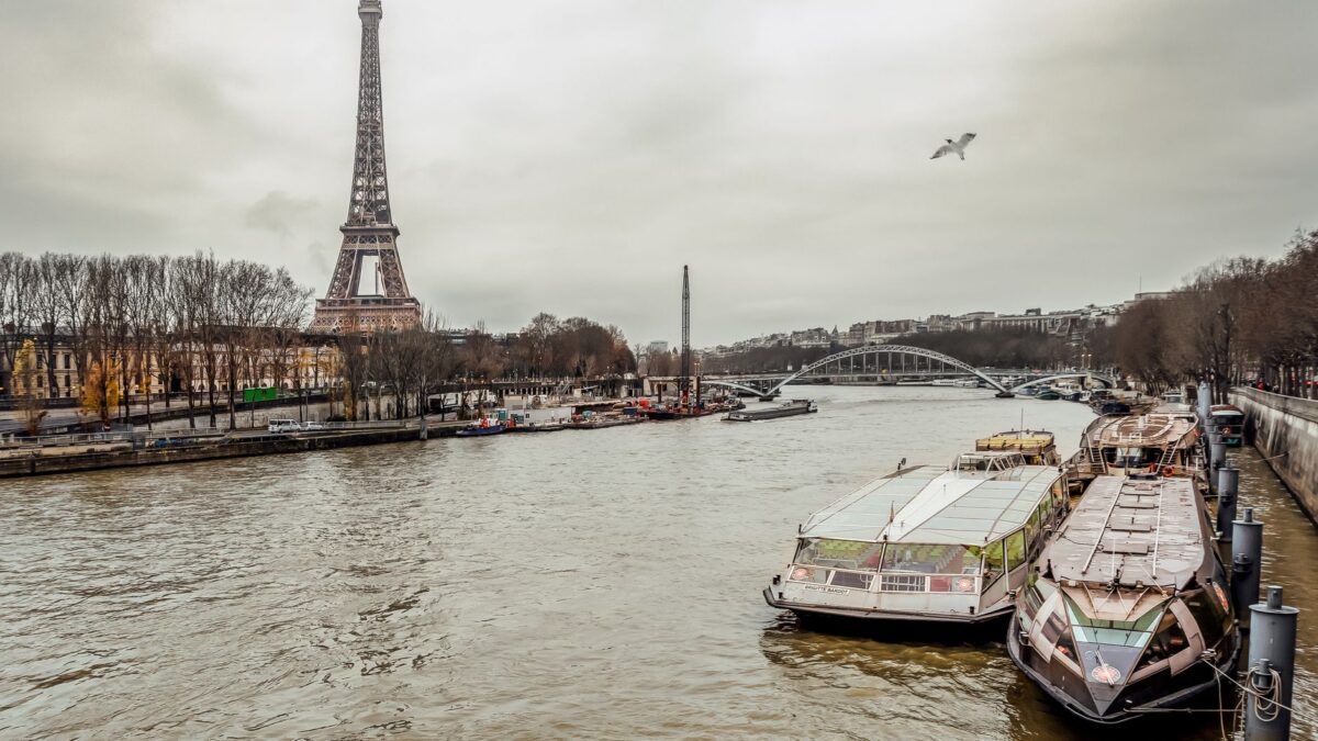 Scenic view of the Eiffel Tower and Seine River with moored boats on a cloudy day.