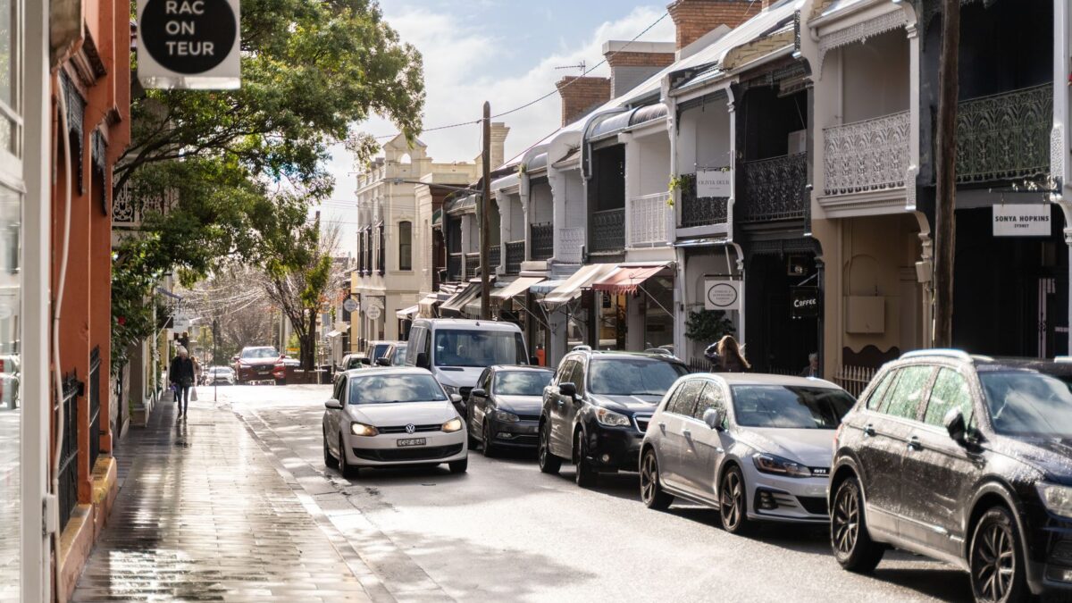 A bustling urban street with parked cars, pedestrians, and charming architectural details.