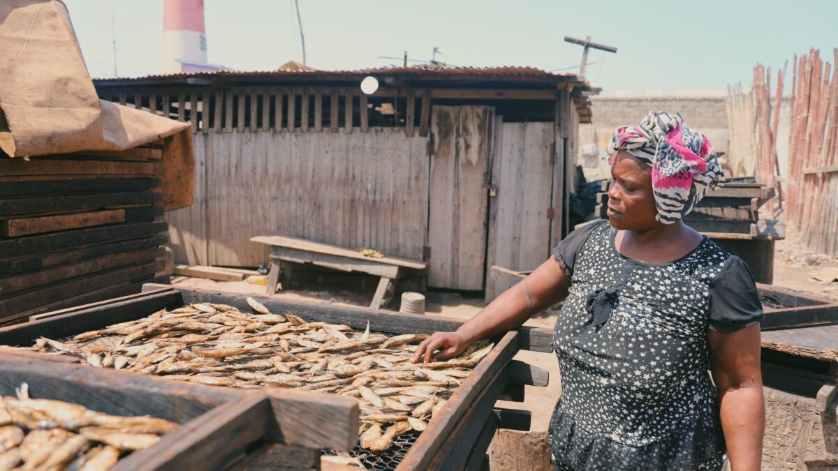 A woman smokes fish outdoors in Accra, showcasing traditional Ghanaian methods.