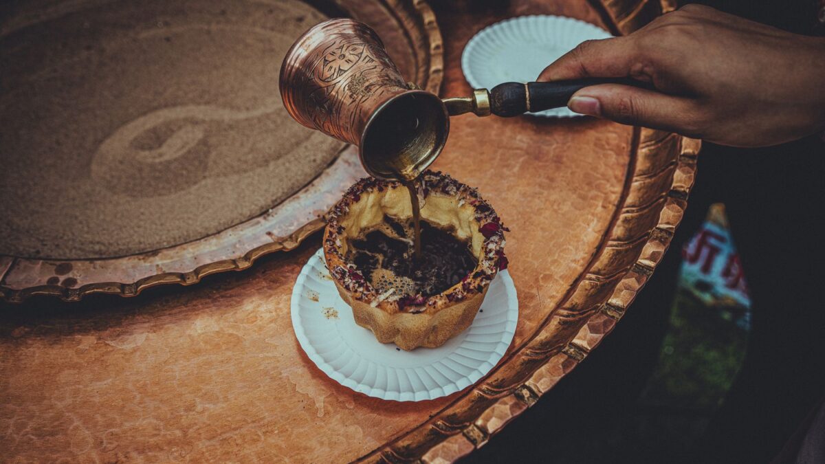 A hand pours traditional Turkish coffee into a cup on a copper tray. Authentic cultural experience.