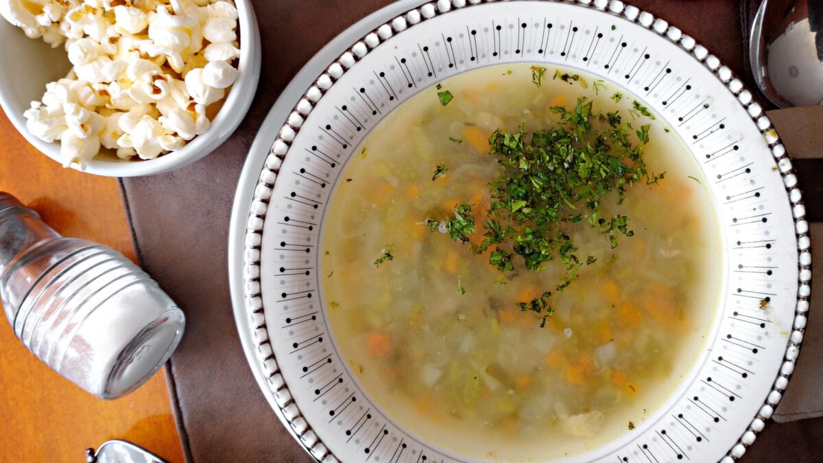 Delicious vegetable soup garnished with herbs accompanied by a bowl of popcorn on a wooden table.