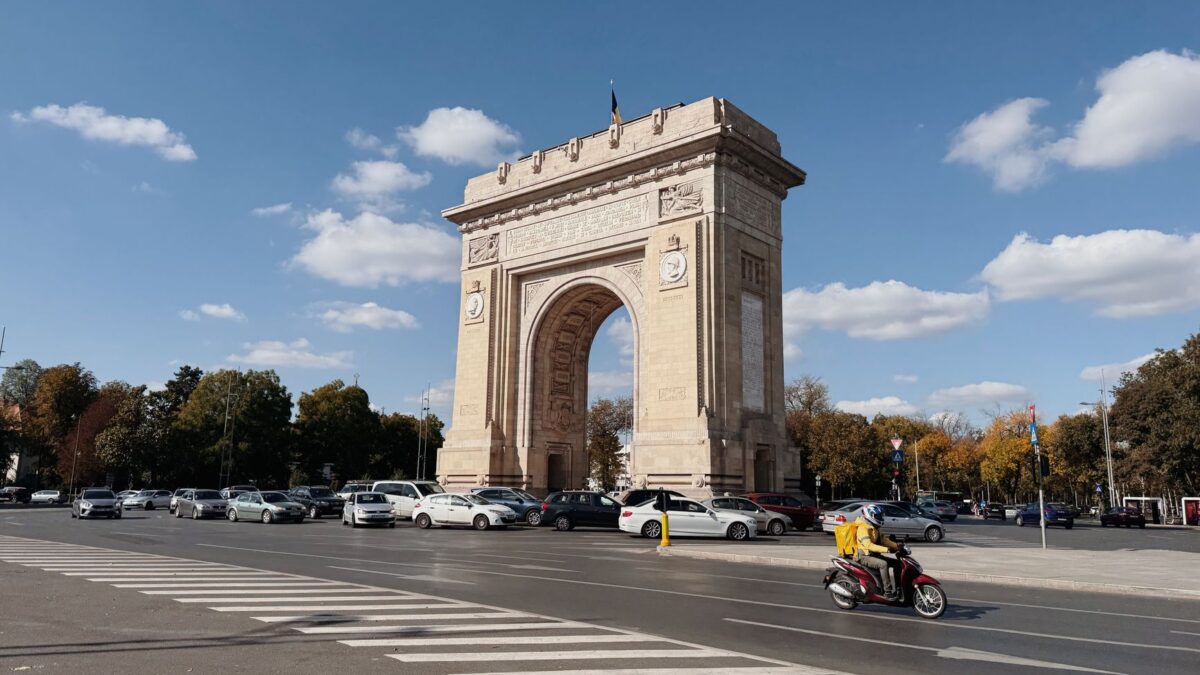 Triumphal arch in Bucharest against a blue sky, with traffic passing by.