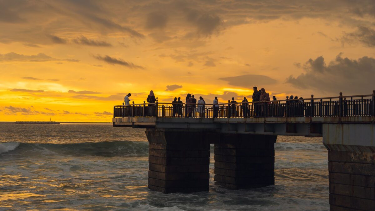 People enjoying the sunset view from a pier in Colombo, Sri Lanka with ocean waves and dramatic skies.