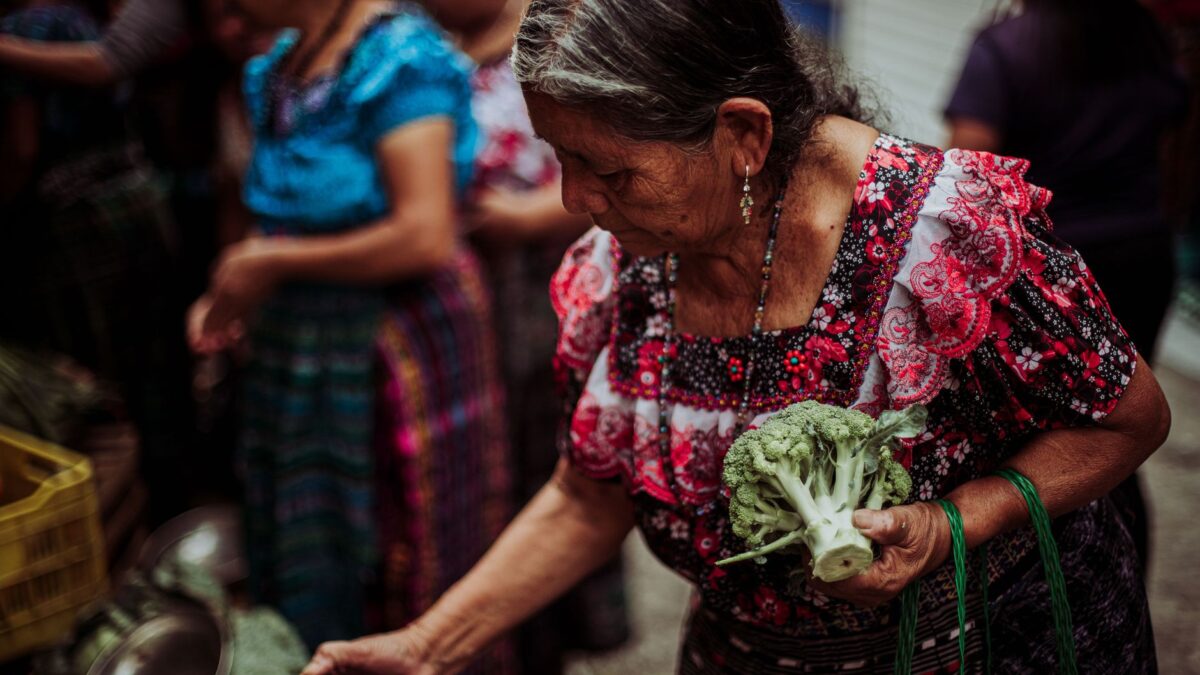 Senior woman in traditional dress shopping for vegetables at a bustling street market.