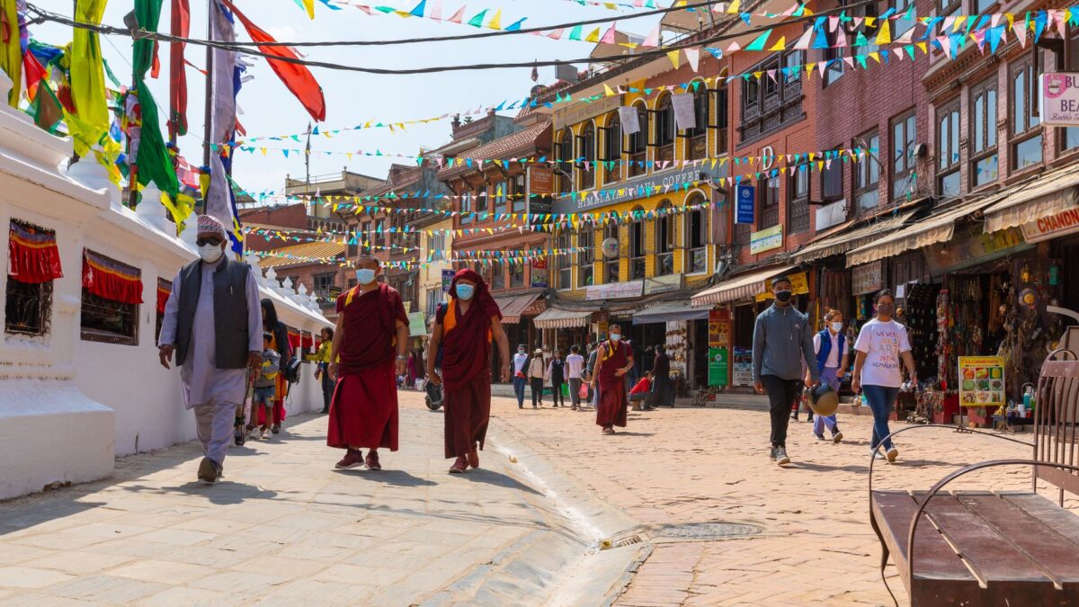 People in colorful attire walk along a decorated street in Kathmandu, Nepal, under festival flags.