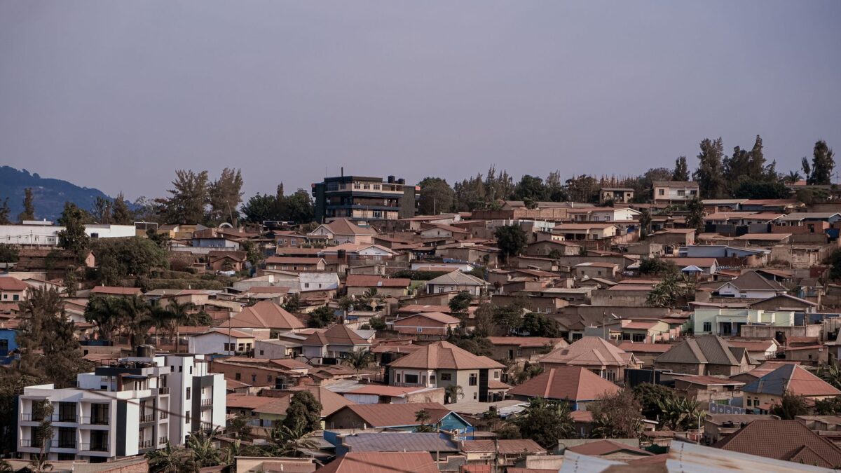 Scenic aerial view of dense urban rooftops against a picturesque hilly backdrop under a clear sky.