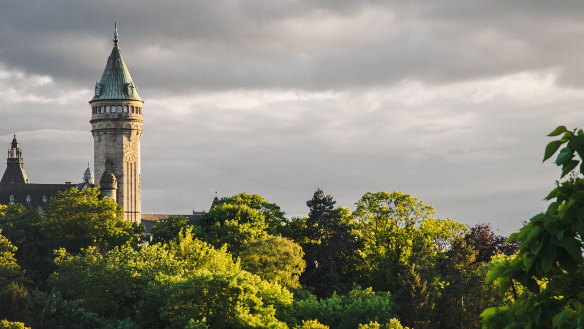 A captivating view of a castle tower in Luxembourg framed by lush green trees and dramatic skies.