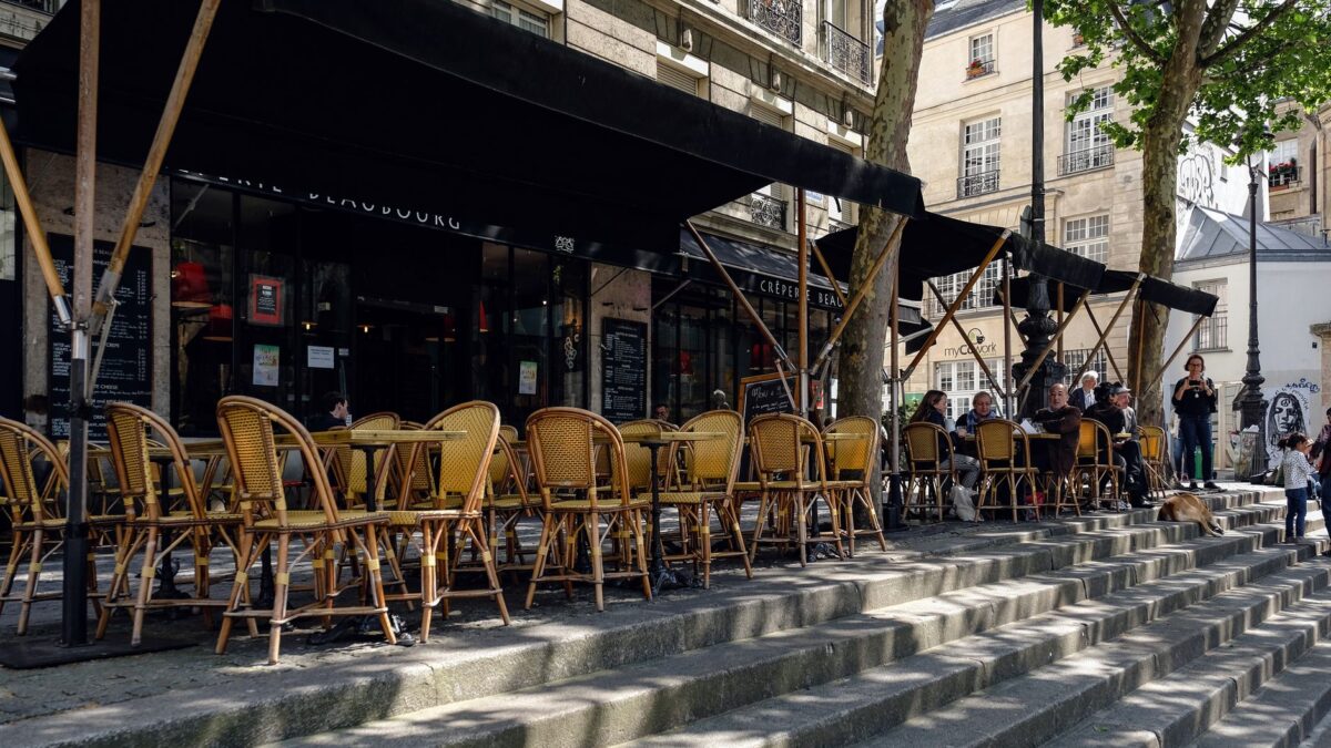 Outdoor Paris café with wicker chairs and people enjoying a sunny day on stone steps.