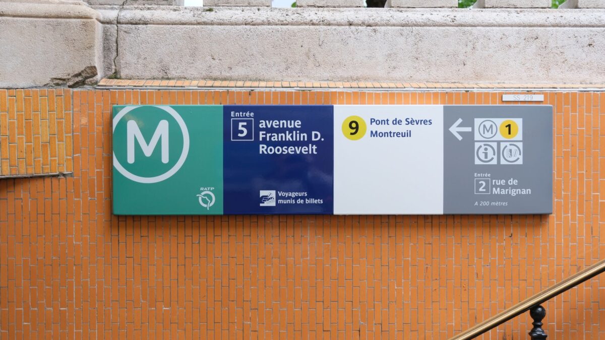 Close-up of a Paris Metro sign at Avenue Franklin D. Roosevelt entrance, featuring directions and route information.