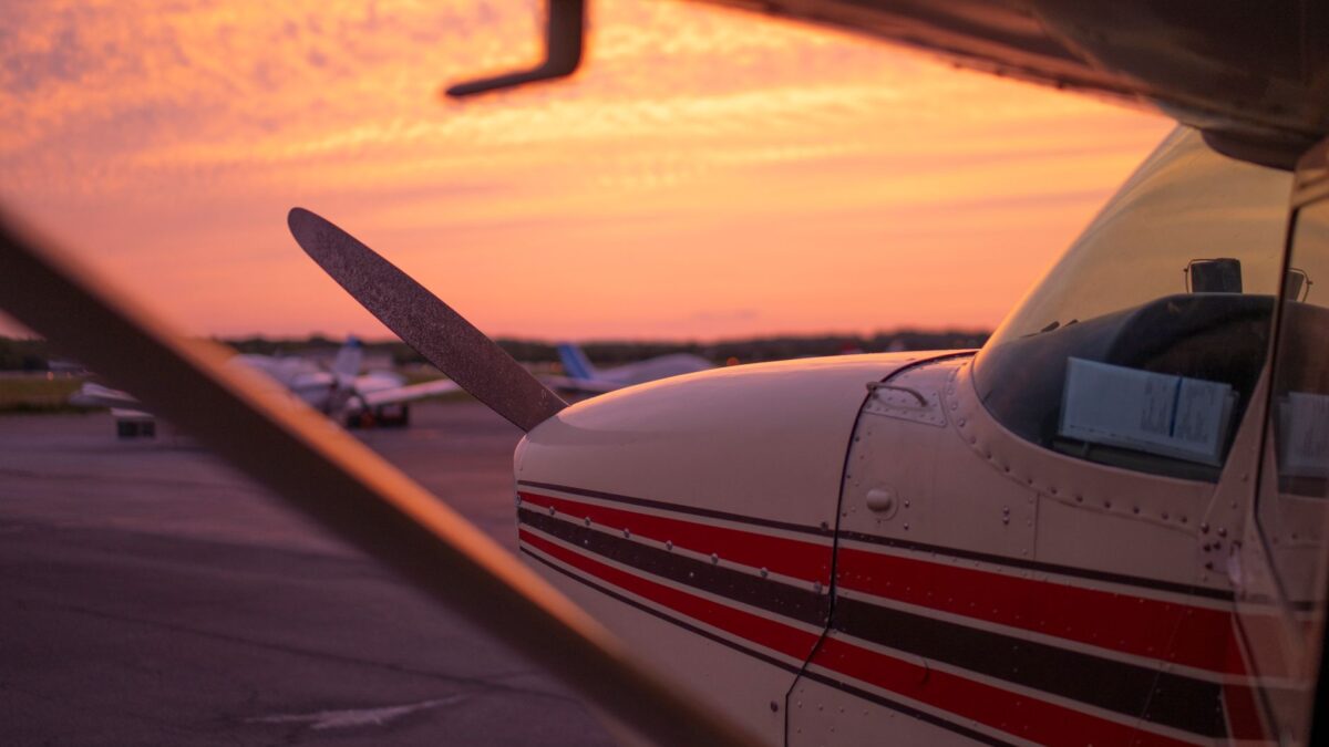 Close-up of a small propeller plane on the tarmac against a vibrant sunset sky, emphasizing aviation beauty.