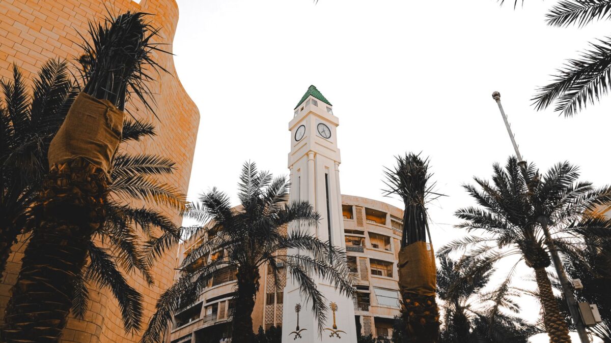 A striking clock tower surrounded by palm trees against a bright sky in an urban environment.