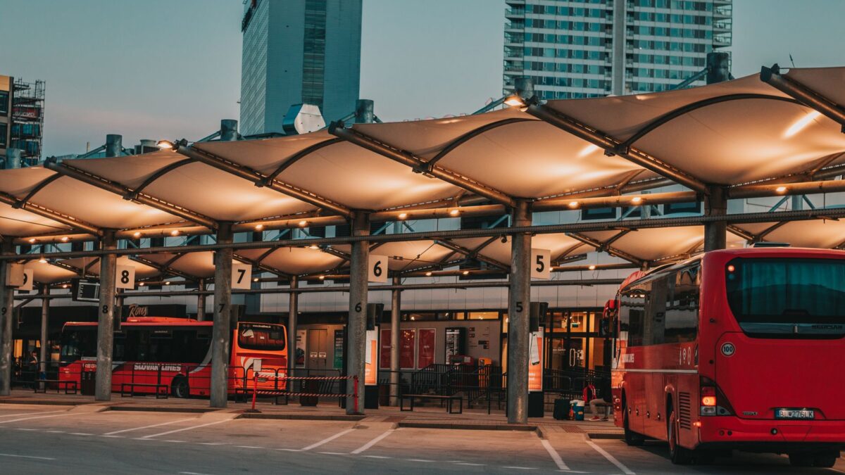 Illuminated bus station with parked buses in an urban setting at dusk.