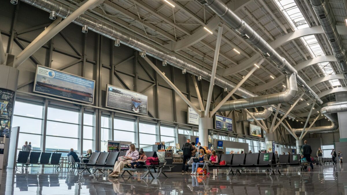 Spacious airport terminal interior with passengers seated and walking, showcasing modern design and large windows.