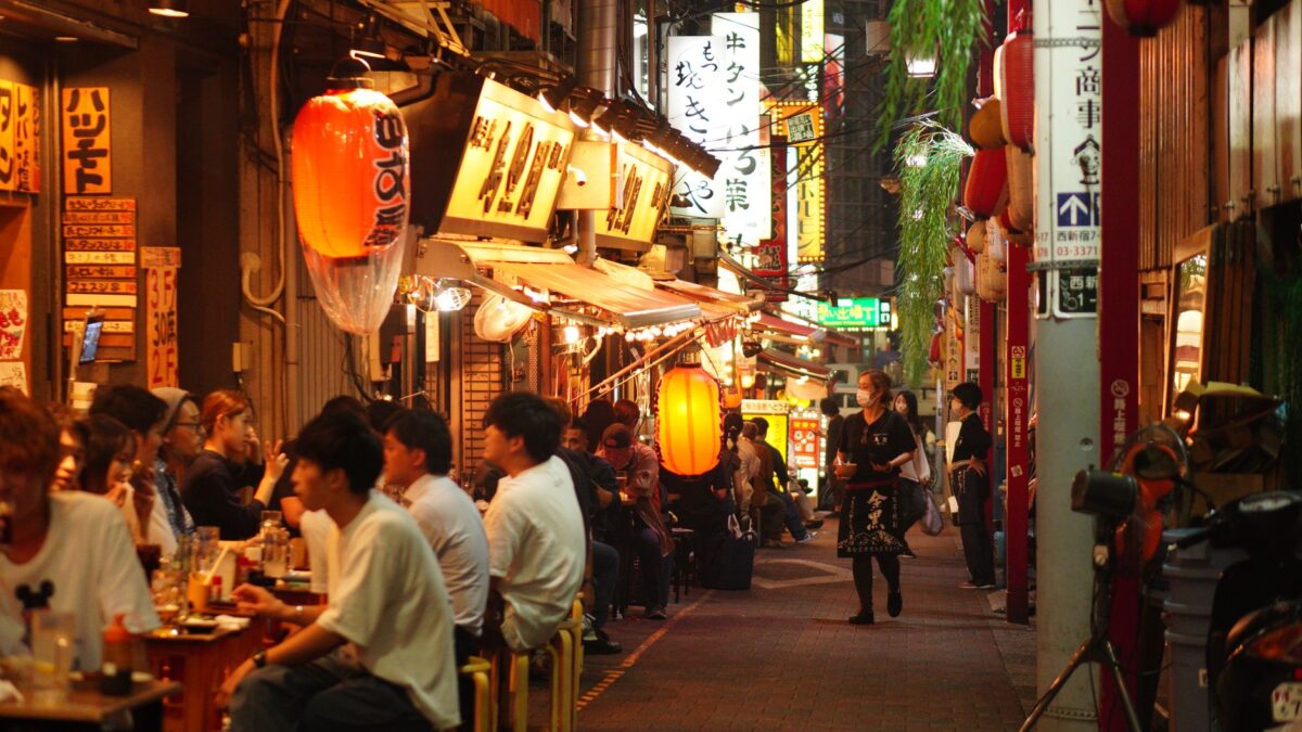 Night scene of people dining in a lively alley in Shinjuku City, Tokyo, illuminated by paper lanterns.