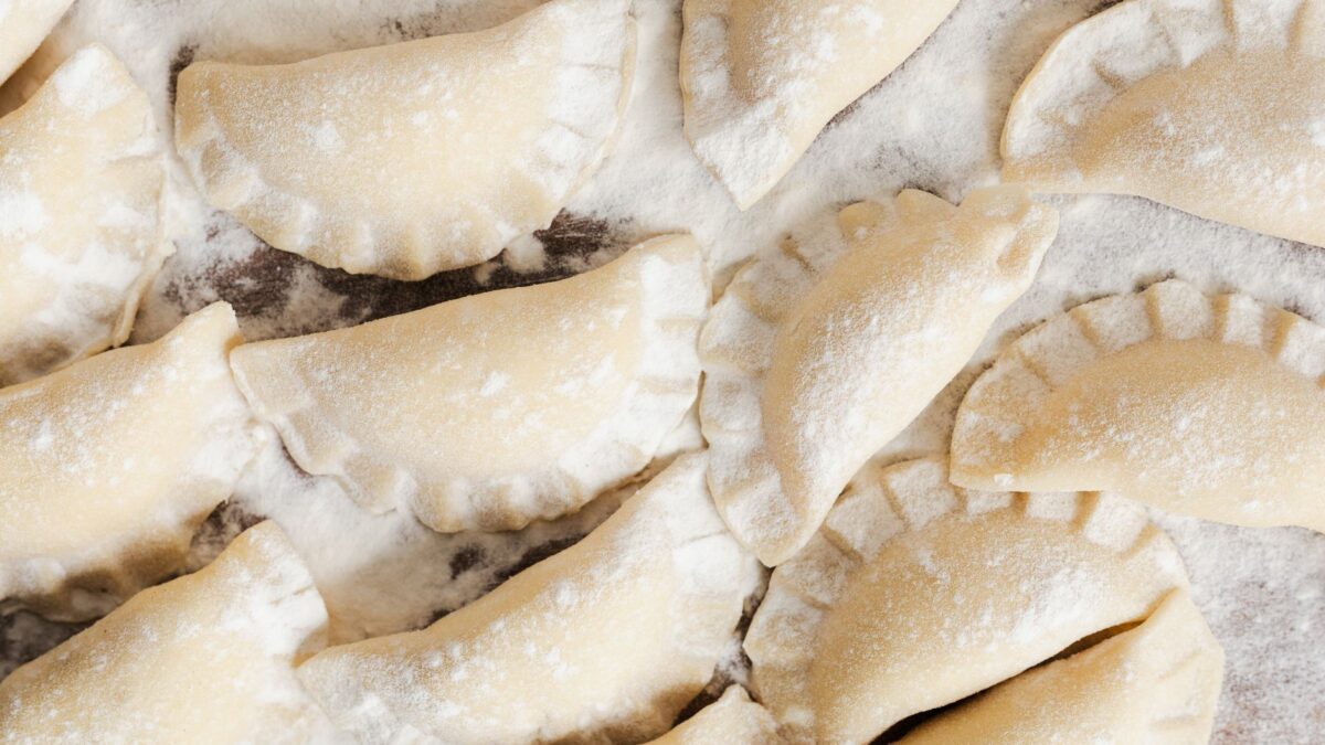Top view of uncooked pierogi dumplings arranged on a floured surface, ready to cook.