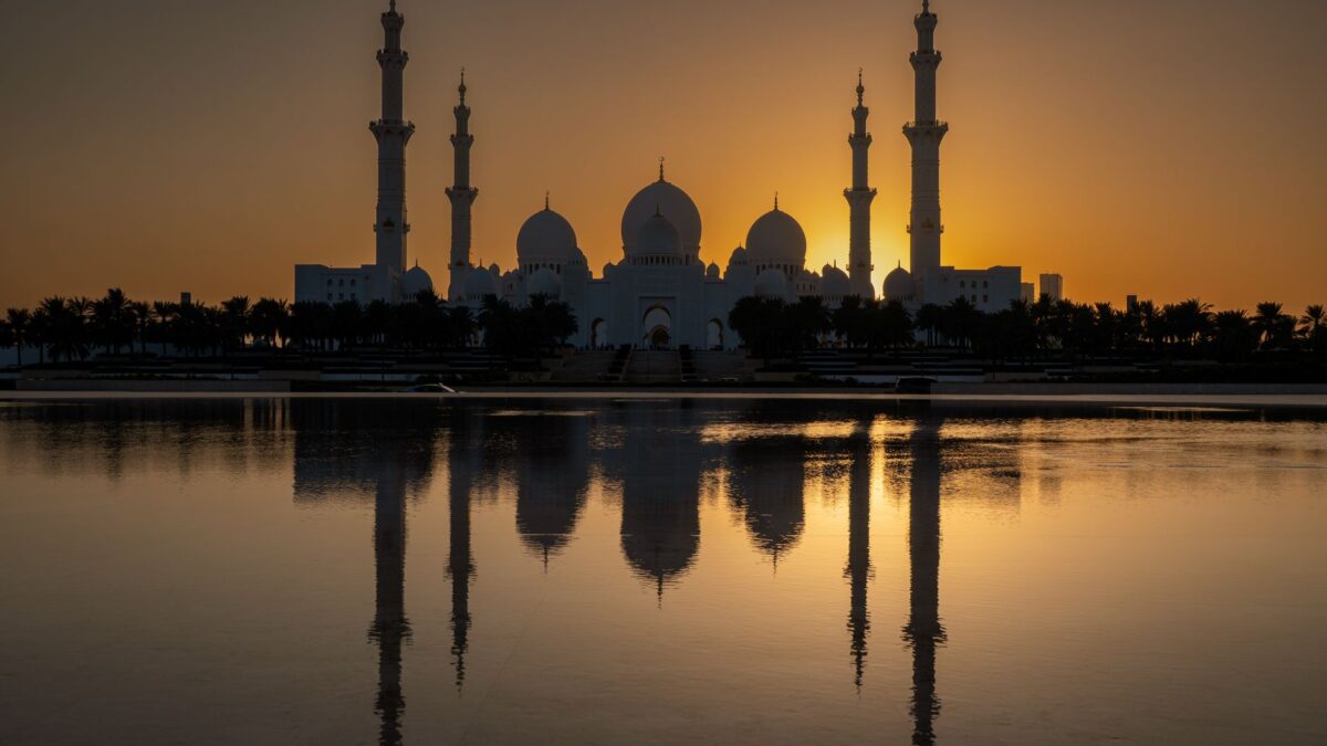 Stunning view of Sheikh Zayed Mosque with sunset reflection in water.