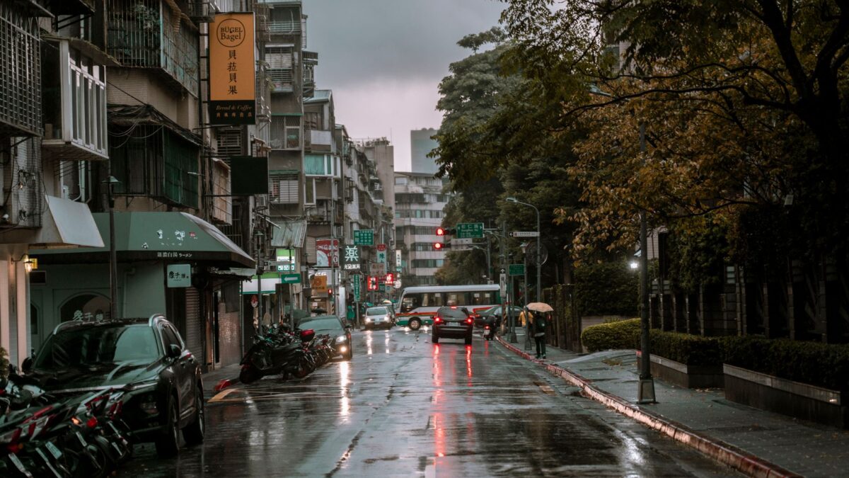 A rainy day on a bustling urban street with cars, pedestrians, and wet pavement.