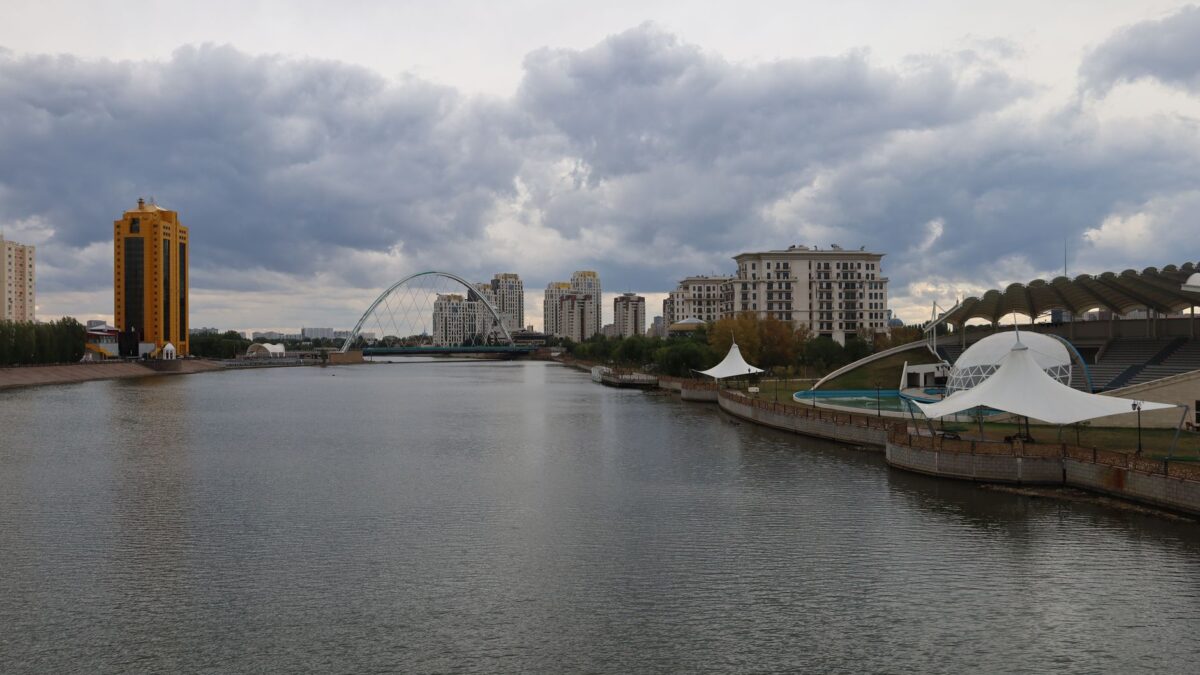 Modern skyline of Astana with residential buildings along the Ishim River under cloudy skies.