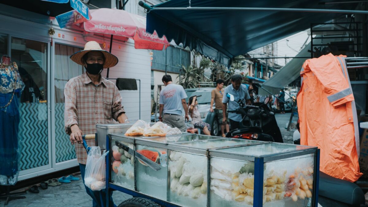 A vendor sells fresh fruit from a cart in a vibrant Bangkok street market.