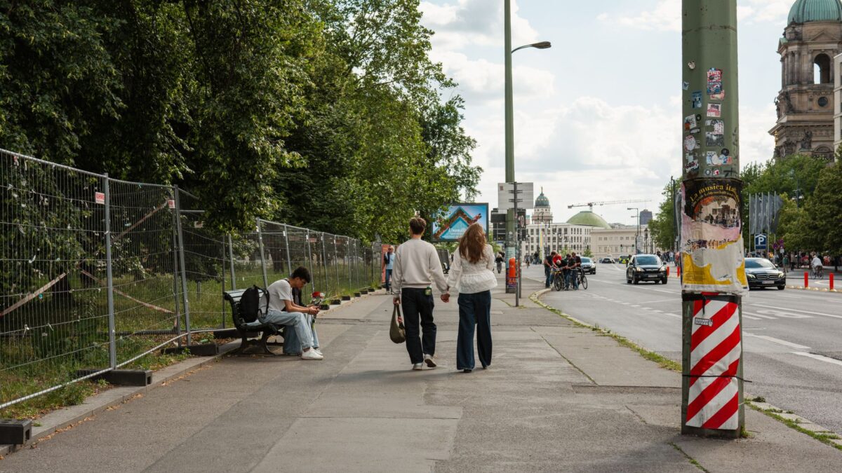 A couple walking along a street in Berlin with the Berlin Cathedral in the background.