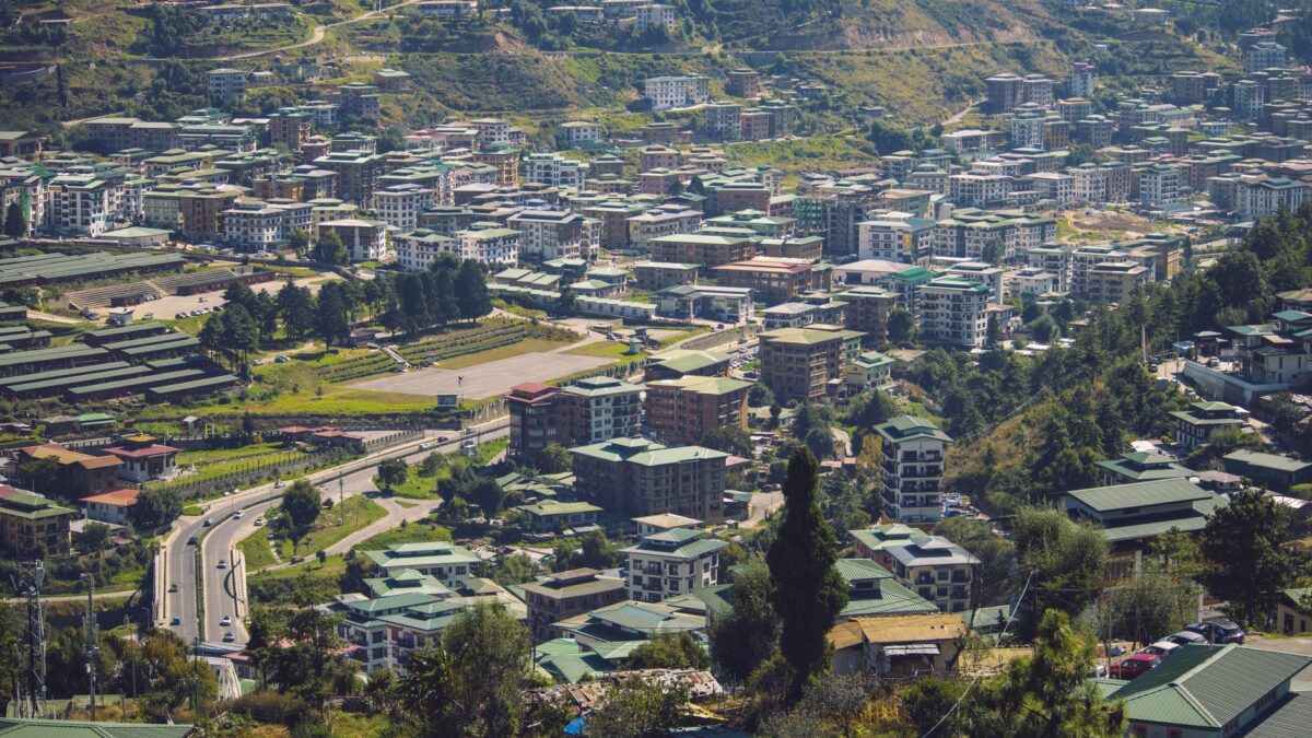 Explore the vibrant cityscape of Thimphu, Bhutan, with dense buildings nestled in lush hills.