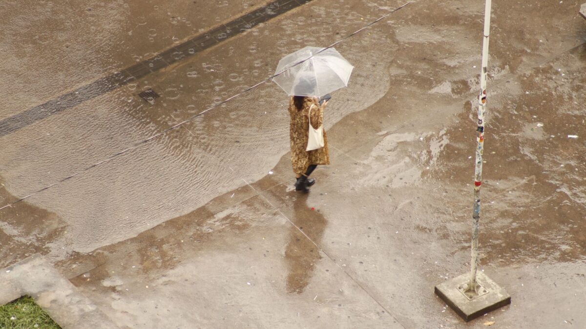 Aerial view of a woman with an umbrella walking on a wet pavement during rainfall.