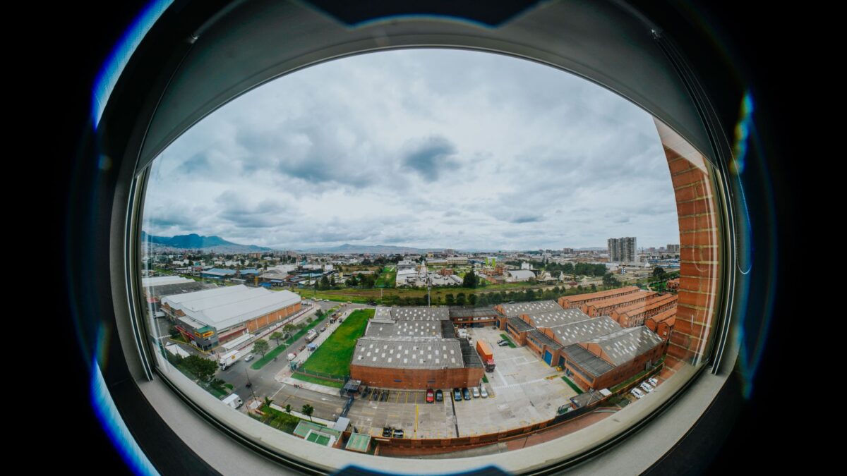 A fisheye perspective capturing Bogotá's urban landscape through a circular window, highlighting an industrial area.