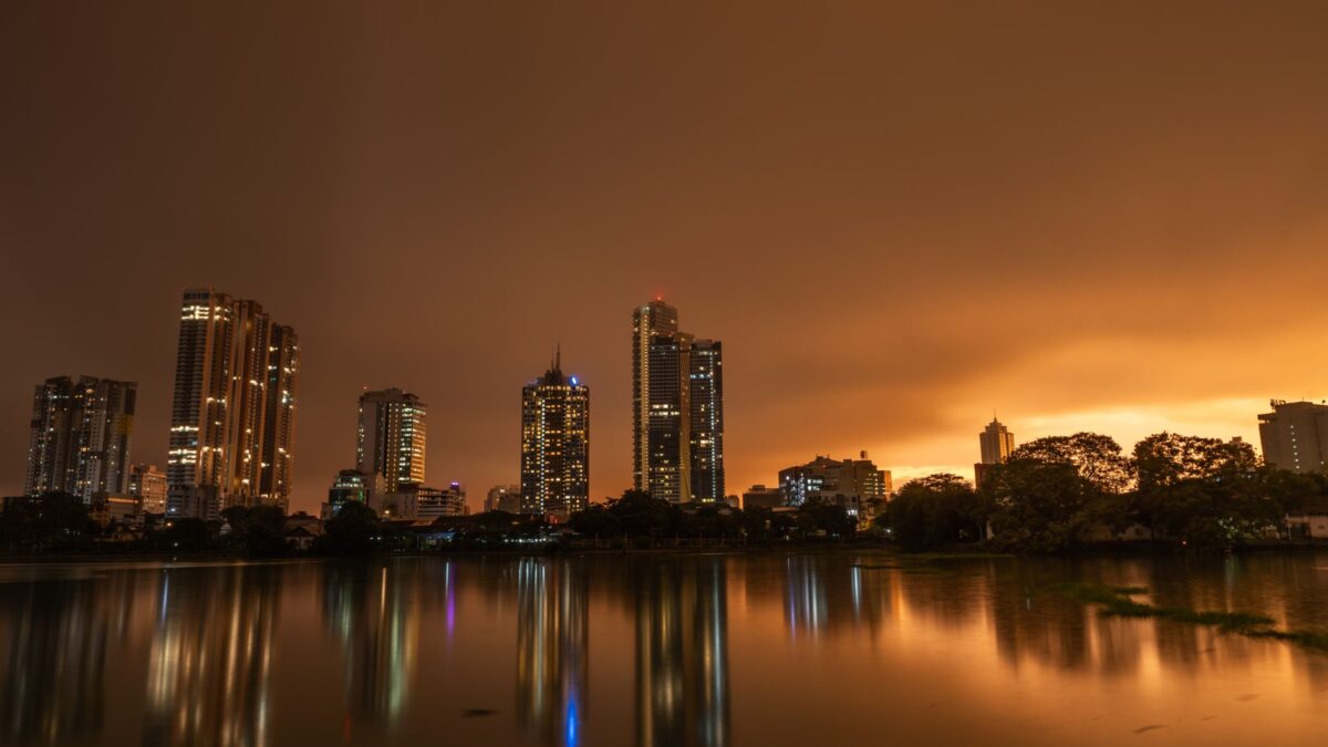 Dramatic twilight skyline of Colombo, Sri Lanka with city lights reflected on calm lake waters.