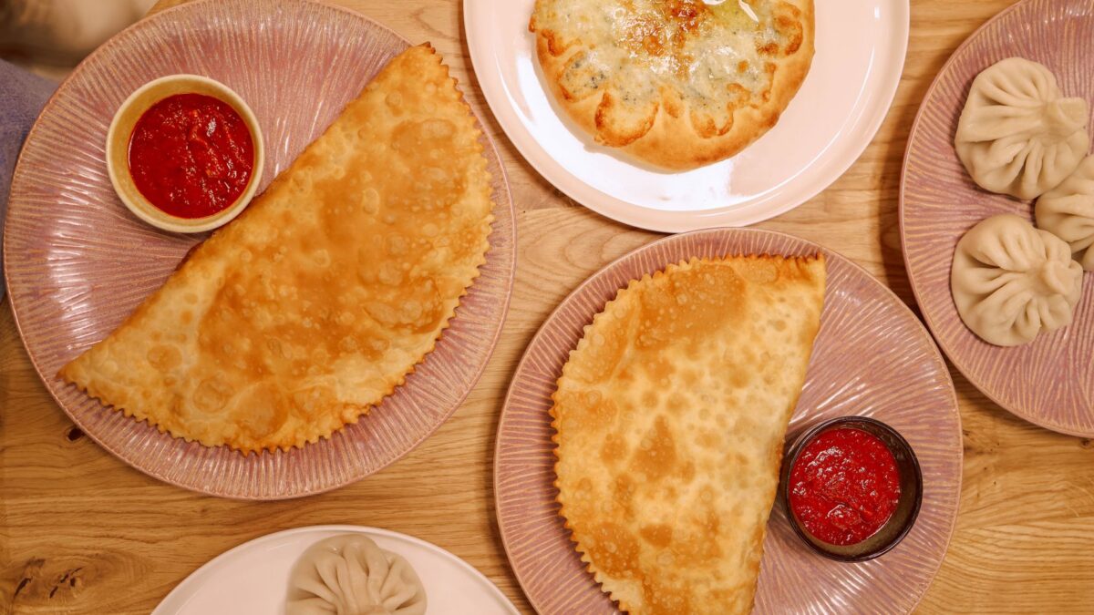 Flat lay featuring khinkali, fried pastry, and cheese bread with dips.