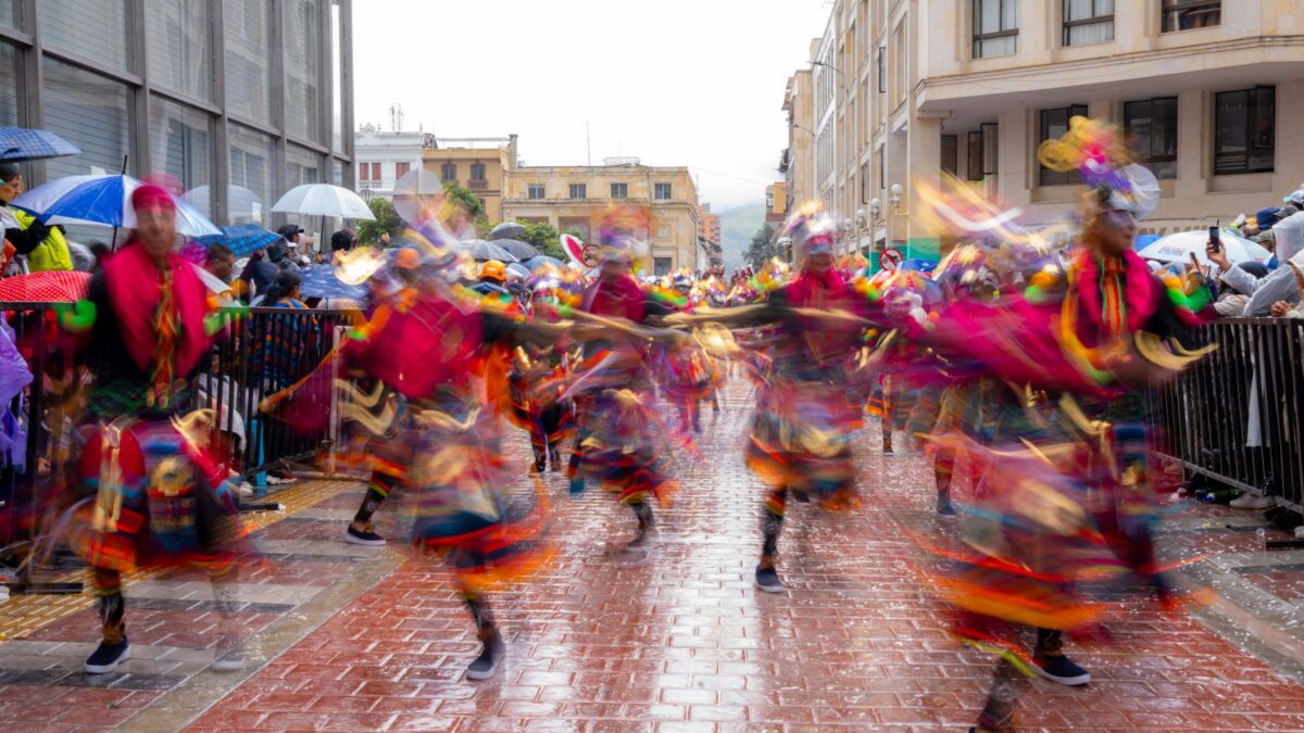 Colorful dancers in traditional costumes performing at a lively street festival on a rainy day.