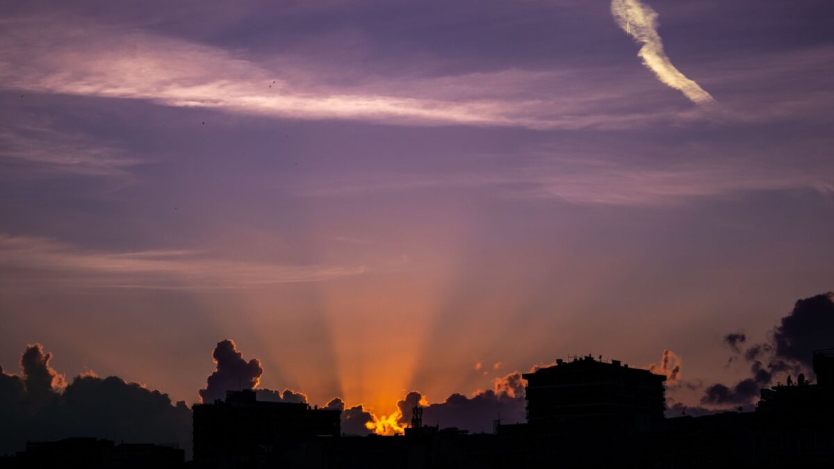 Silhouetted city buildings under a dramatic sunset sky with vibrant colors.