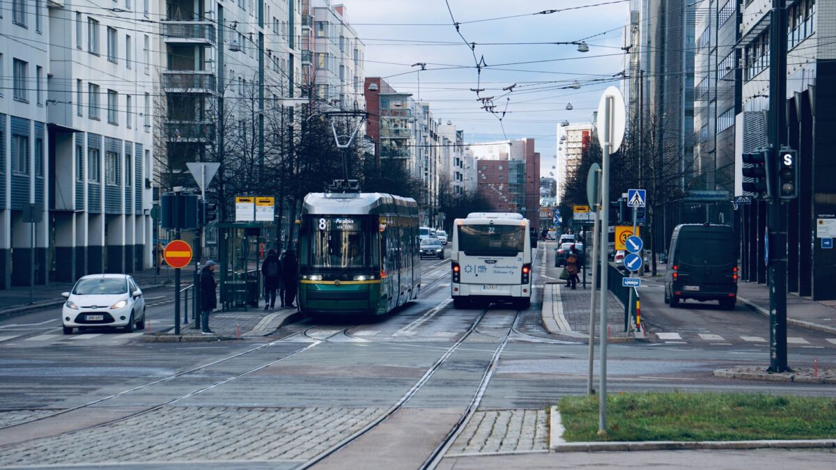 A busy Helsinki street featuring a tram and bus with surrounding urban architecture.