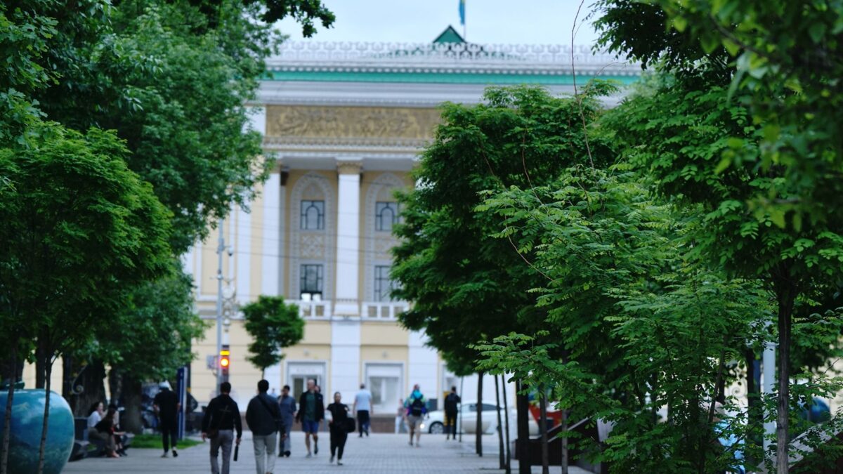Bustling Panfilov Street in Almaty lined with green trees and historical architecture.