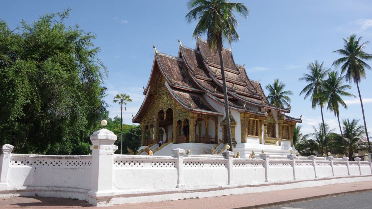 Explore the Royal Palace's intricate architecture surrounded by lush palms in Luang Prabang, Laos.