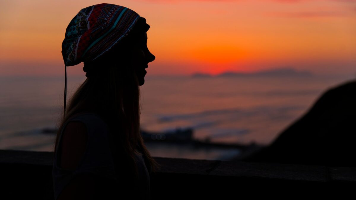 A woman in silhouette wearing a colorful bonnet at sunset in Lima, Peru's coastline.