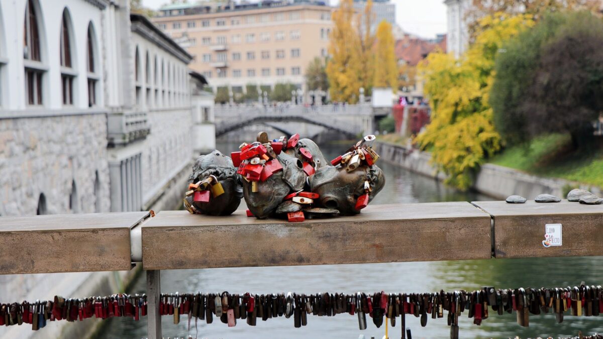 A scenic view of a bridge with love locks over a canal in Ljubljana, Slovenia during autumn.