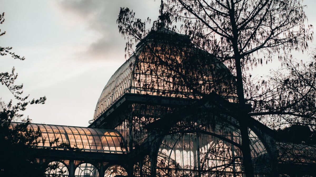 The iconic glass structure of Palacio de Cristal contrasts against a dusky sky in Madrid, Spain.