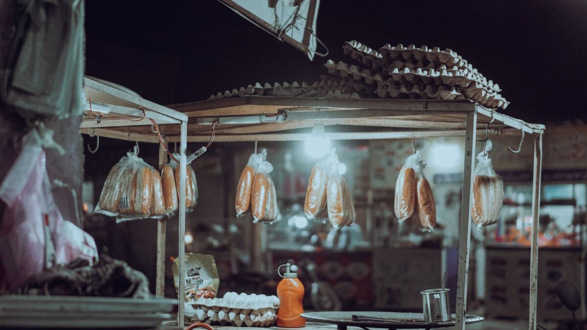 Lively street food stand at night with lights illuminating bread and egg packages.