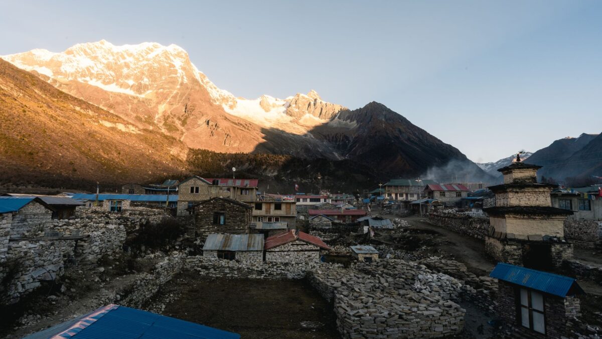 A serene Himalayan village with mountains at sunrise, showcasing rustic architecture in Nepal.