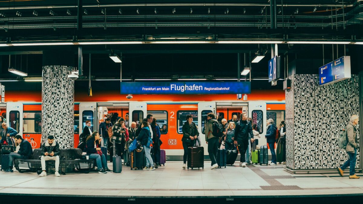 Passengers wait on the platform at Frankfurt am Main Flughafen train station with a regional train in the background.