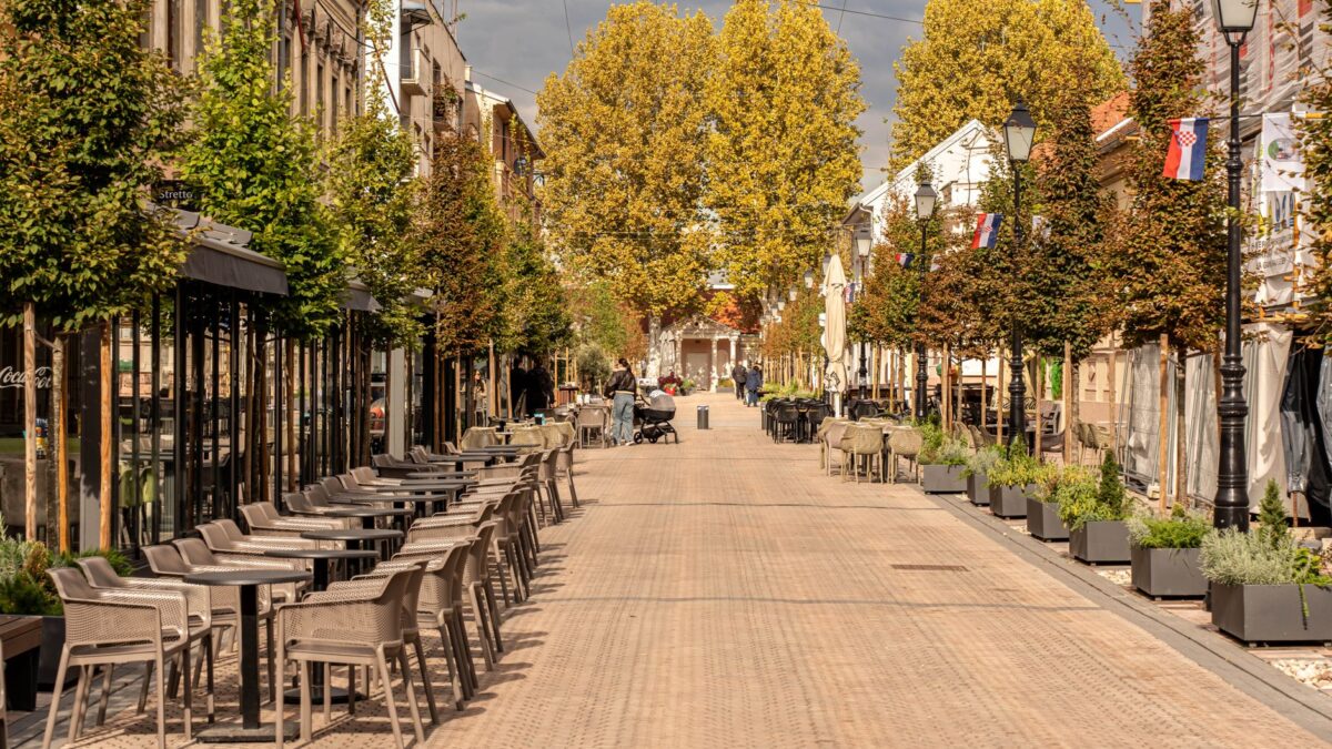 European street during autumn with outdoor cafes and vibrant trees under a cloudy sky.
