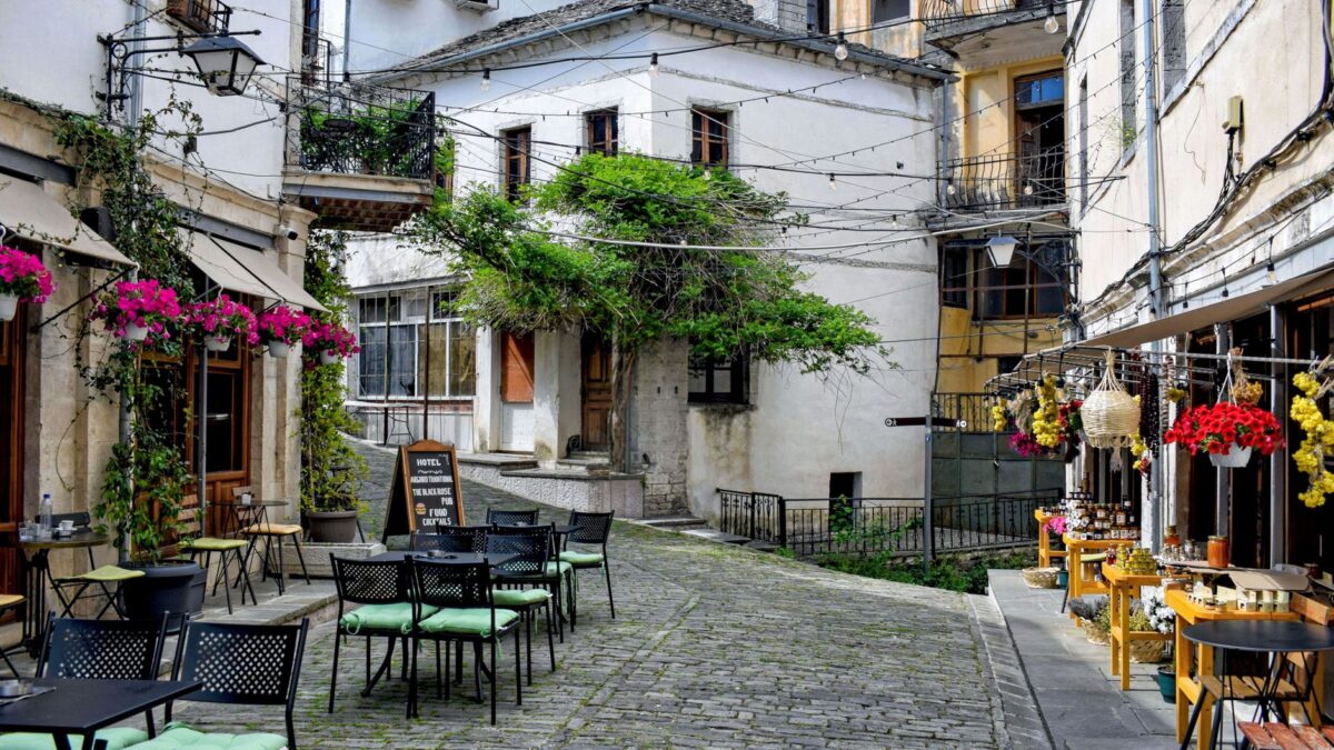 Discover a picturesque street in Gjirokastër, Albania, featuring cozy outdoor cafes and vibrant plants.