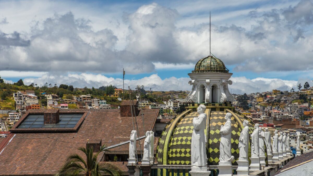 A beautiful architectural dome with statues viewed against an urban backdrop under a vibrant sky.