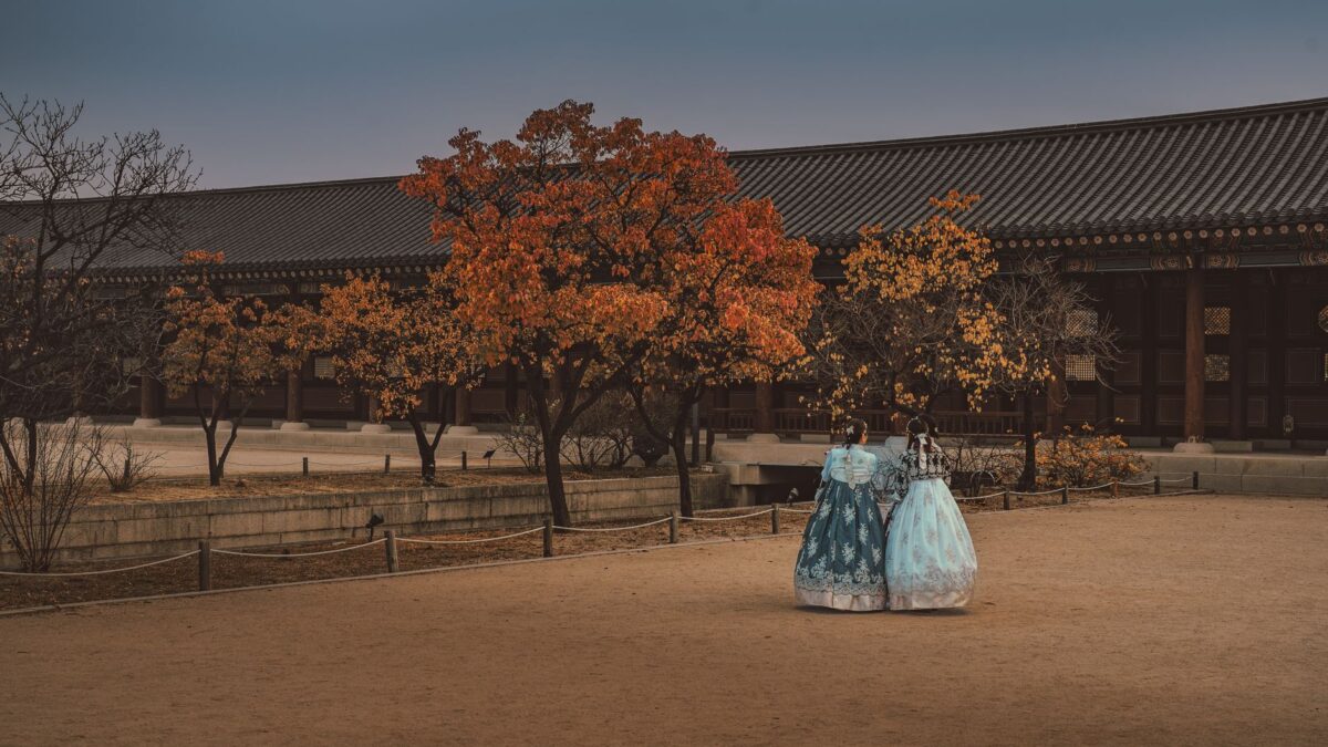 Two women in hanbok stroll through Gyeongbokgung Palace, Seoul, during autumn.