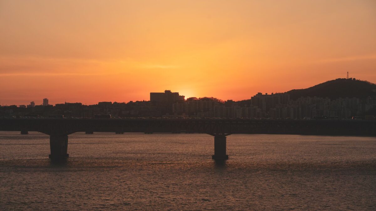 Scenic view of a city skyline at sunset with a bridge over a river.