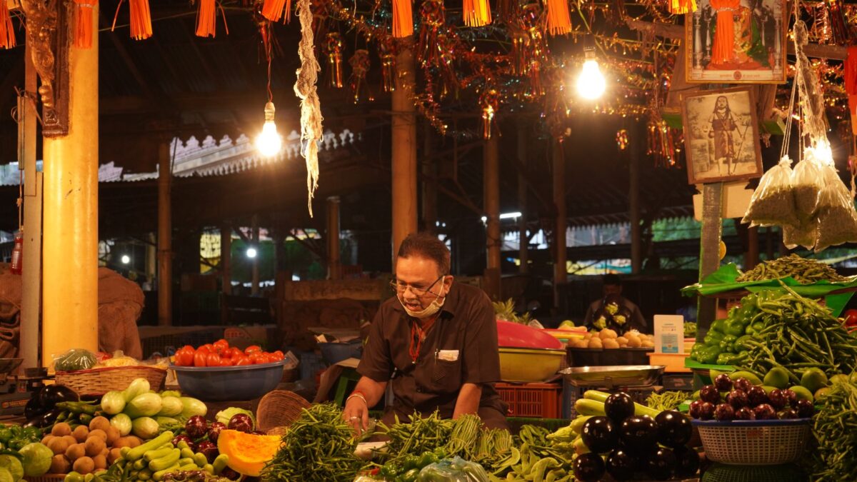 An Indian vendor selling fresh vegetables in a lively bazaar at night.